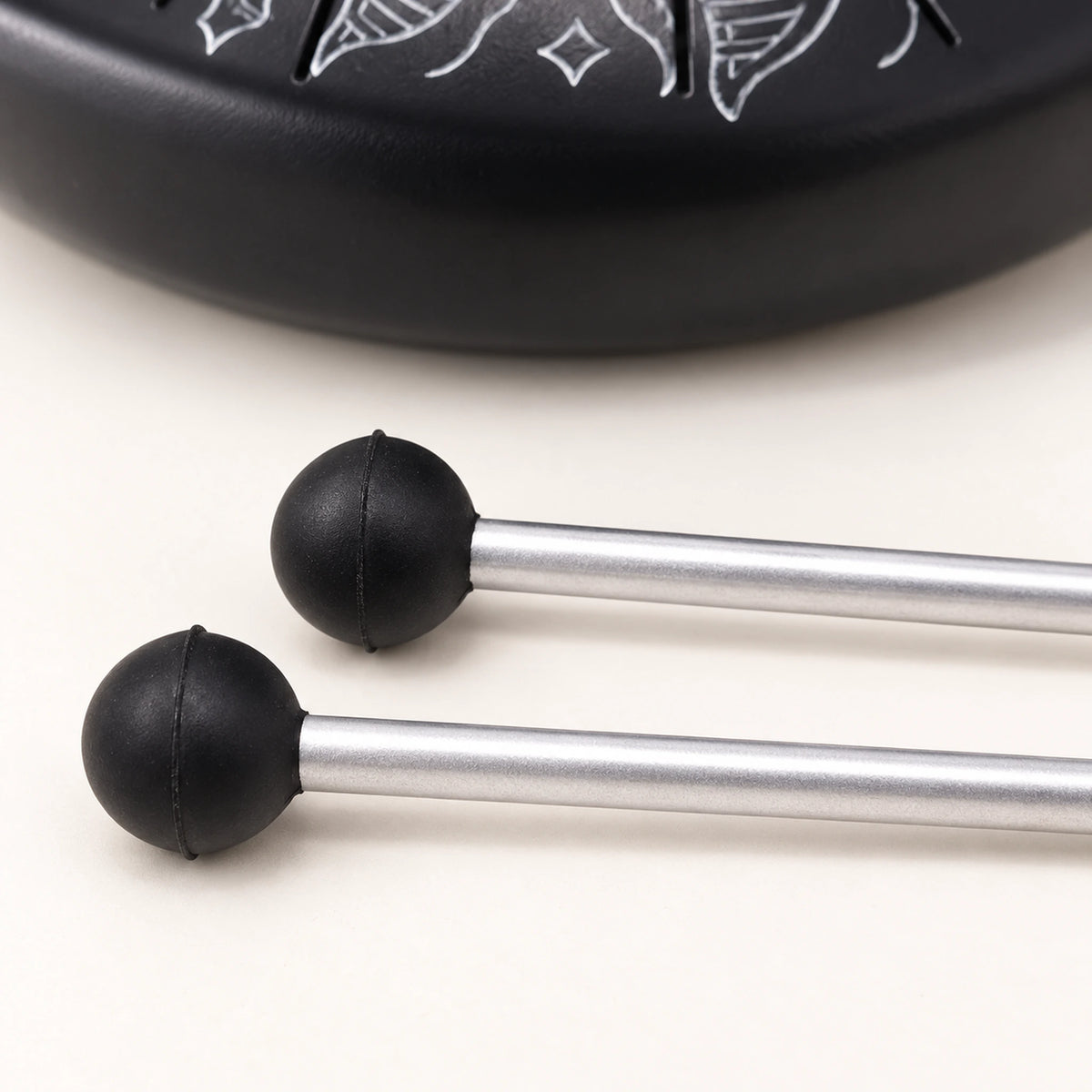 Close view of the two black mallet heads and adjoining silver-coloured shaft sections on an ivory surface.