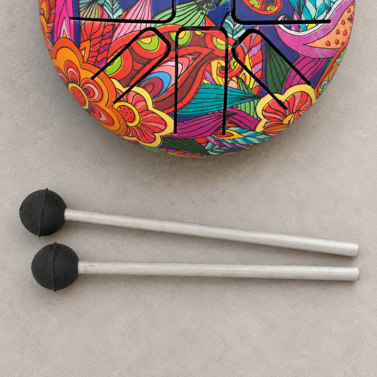 Two mallets with rounded black heads and pale shafts beside a cropped section of the colourful Happy Drum.