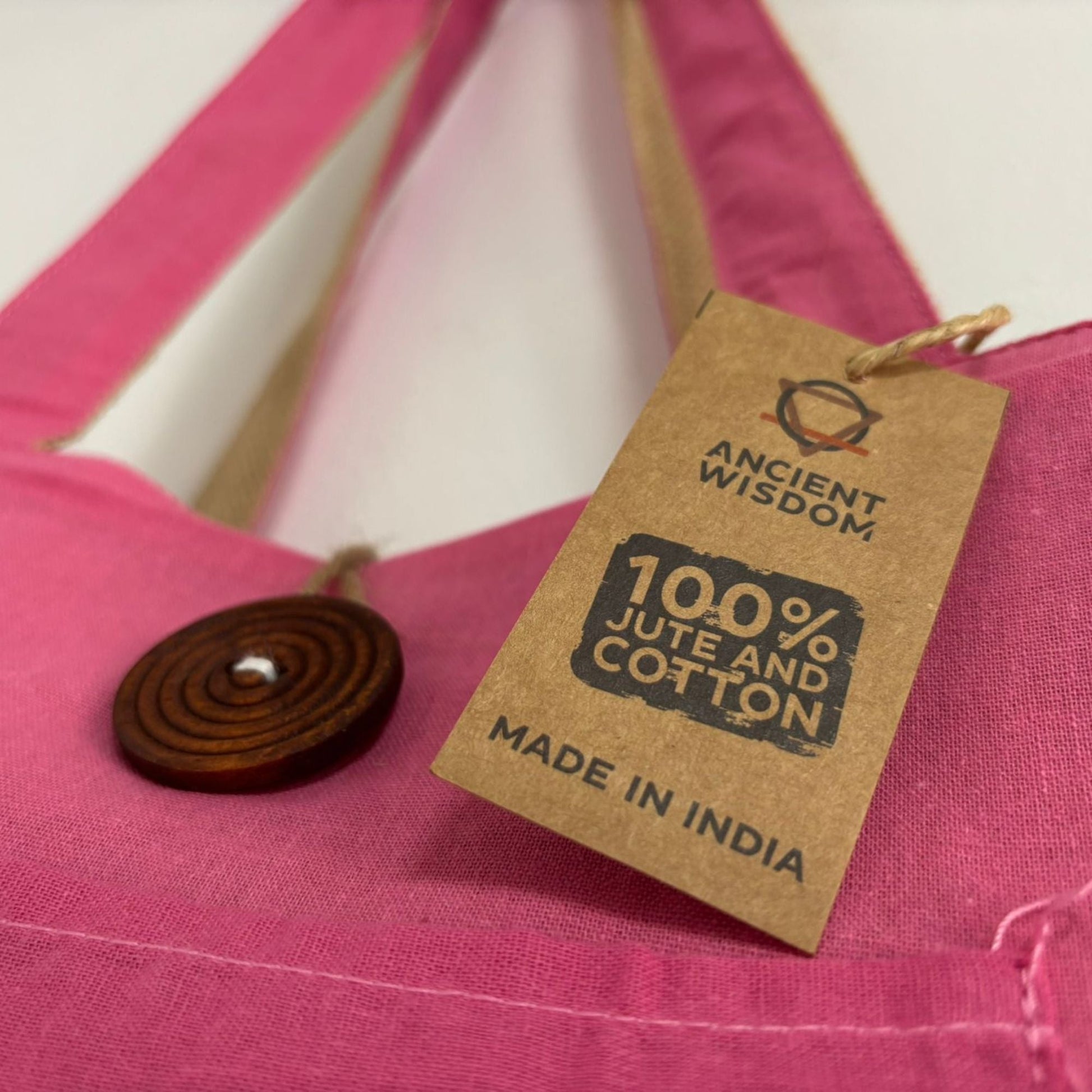 Eco-Chic Reversible Jute & Cotton Bag – Pink, close-up of pink cotton tote with wooden button and tag reading 100% jute and cotton