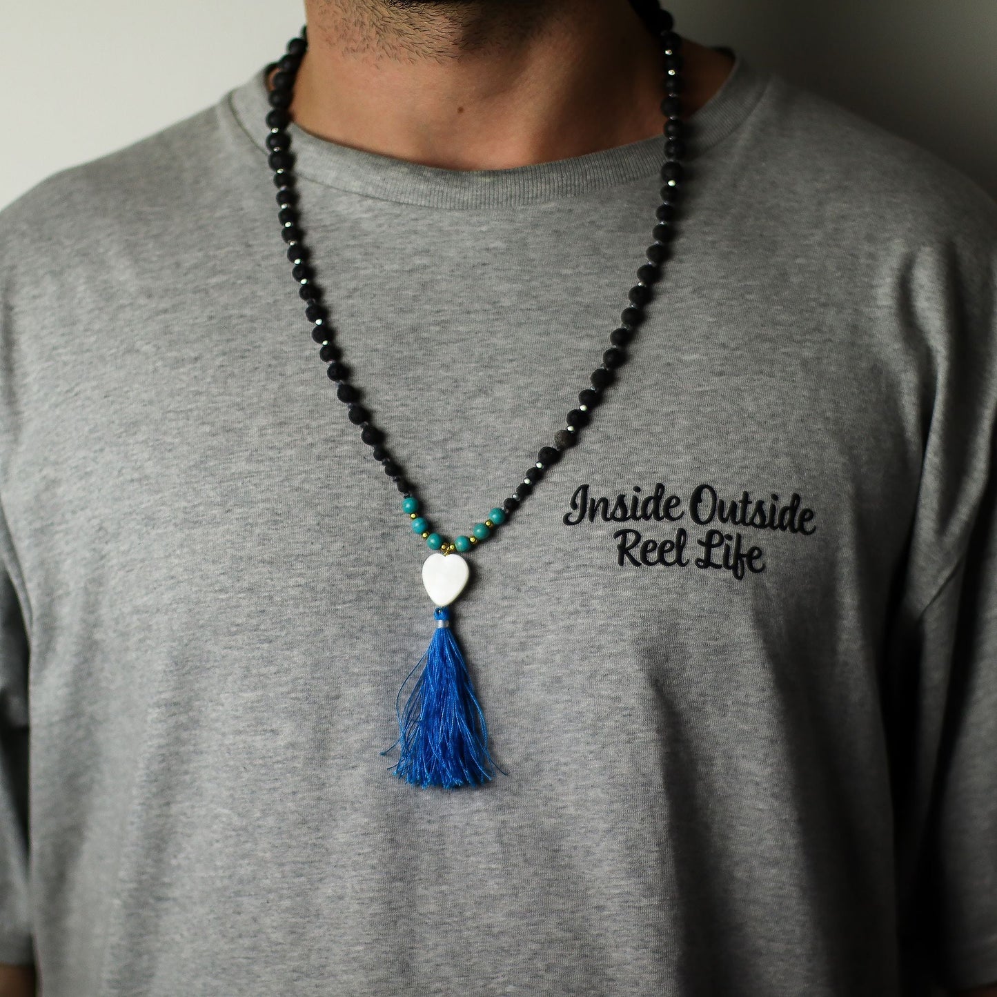 Essence of the Volcano Necklace – Calming Influence black lava stone bead necklace with turquoise accents, white heart charm and blue tassel