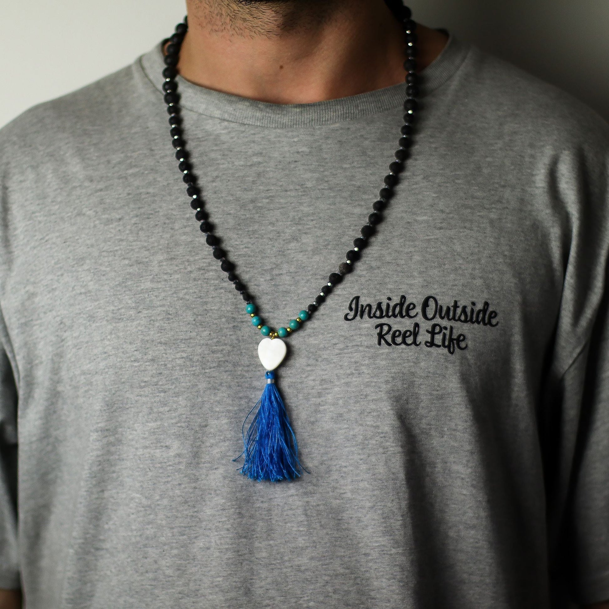 Essence of the Volcano Necklace – Calming Influence black lava stone bead necklace with turquoise accents, white heart charm and blue tassel