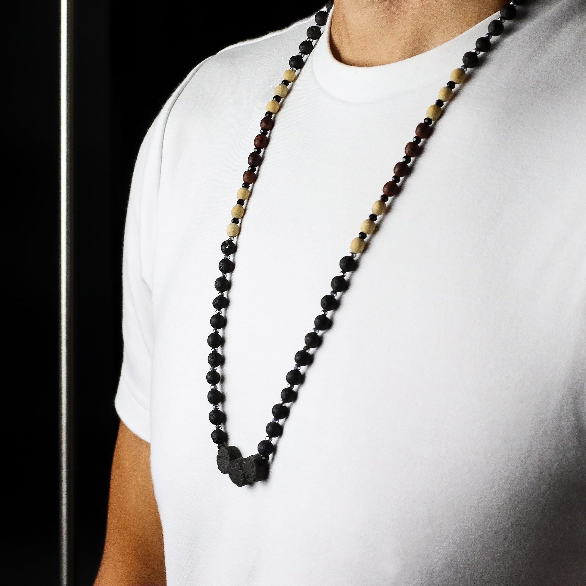 Alt Tag: Essence of the Volcano Necklace – Kontakt med naturen, långt halsband med svarta lavapärlor och jordtoner på modell med vit t-shirt