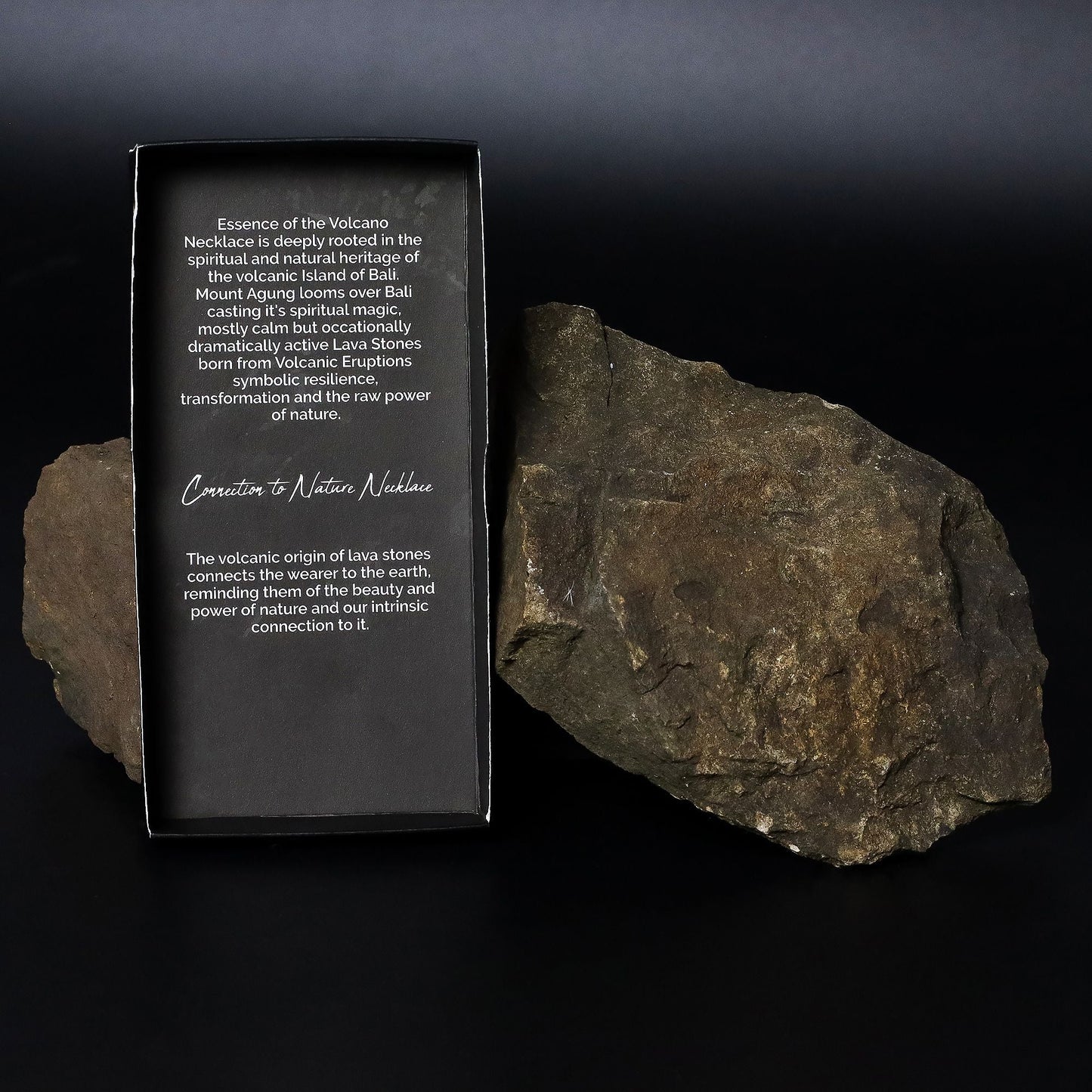 Alt-tagg: Essence of the Volcano-halsband – koppling till naturen produktförpackning bredvid naturlig vulkansten på mörk bakgrund