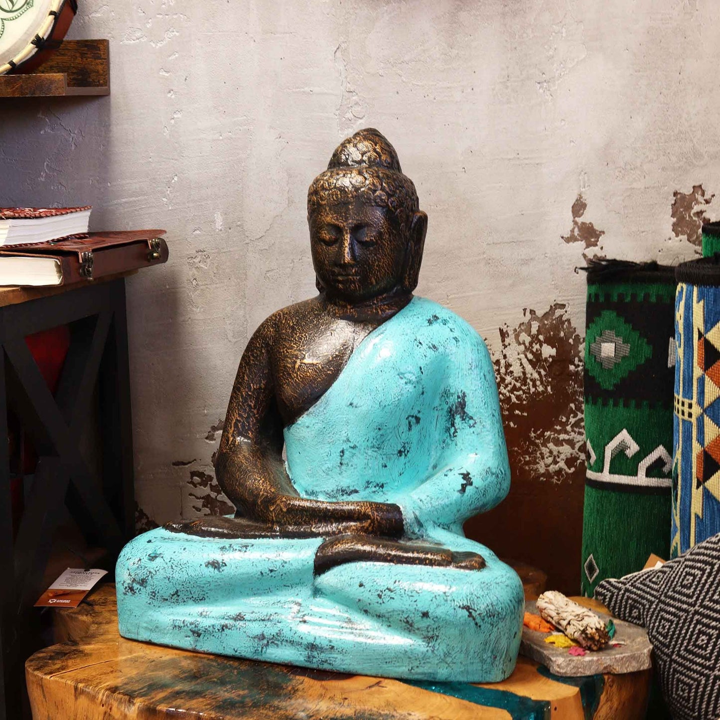 Alt Tag: Buddha-staty i fibercement – 0,5 m sittande Buddha-staty med turkos kåpa och bronsfinish på ett träbord inomhus