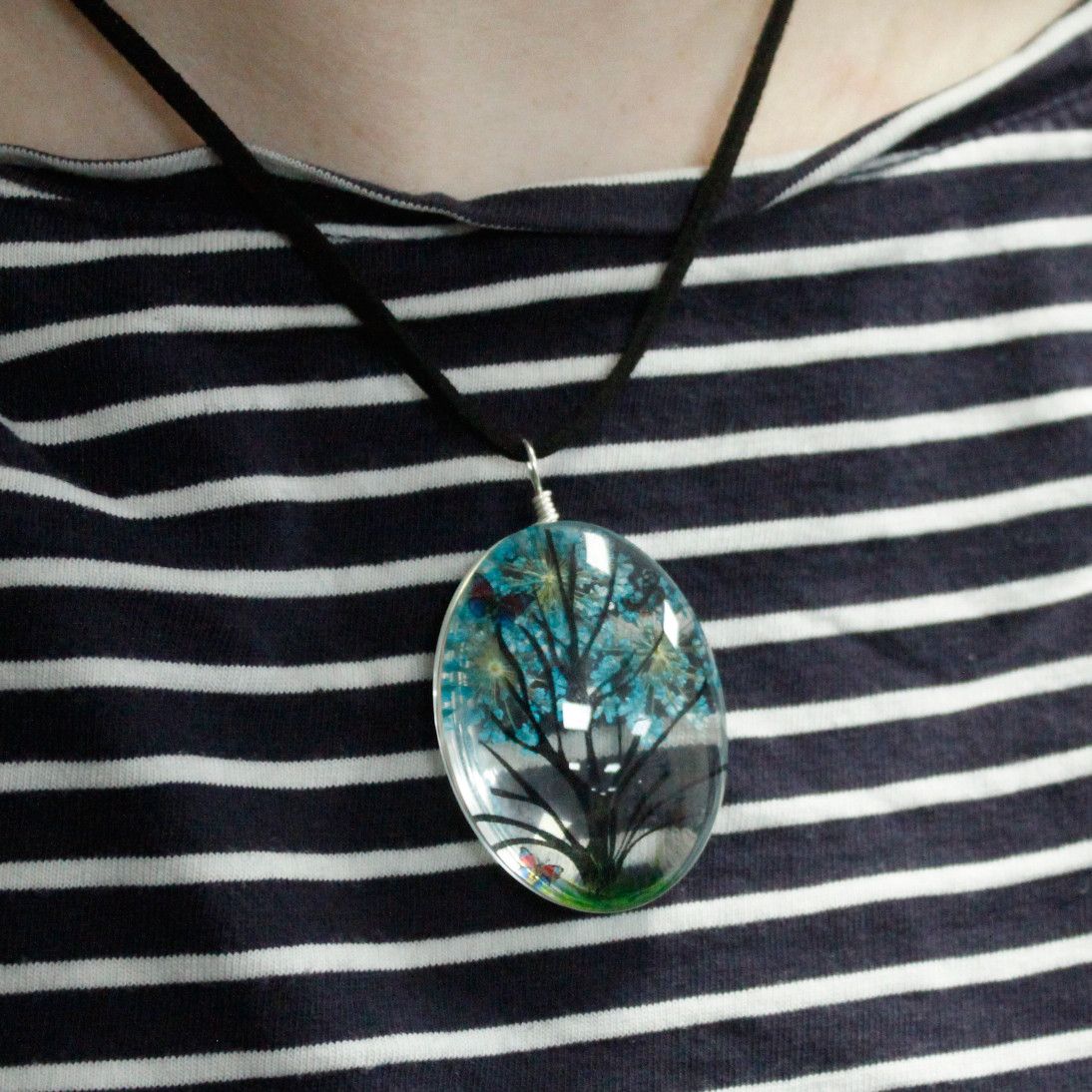 Alt Tag: Glass & Flower Tree of Life Jewellery – Green oval glass pendant necklace with pressed flowers on black cord, worn on striped top
