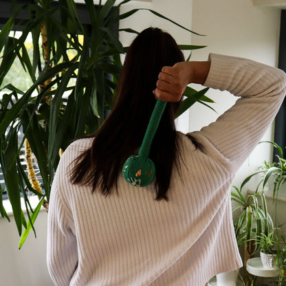 Martillo de masaje de ajenjo verde – Herramienta de madera en uso en la parte superior de la espalda, masajeador percutor de madera con hierbas verdes en su interior sostenido por una persona en interior