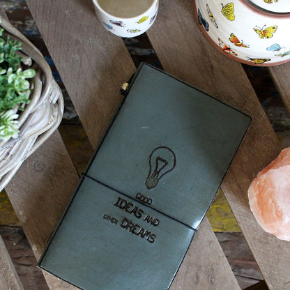 Handcrafted Leather Journal – Black 80 Pages on wooden table with elastic band closure, lightbulb and “Ideas and Dreams” cover design