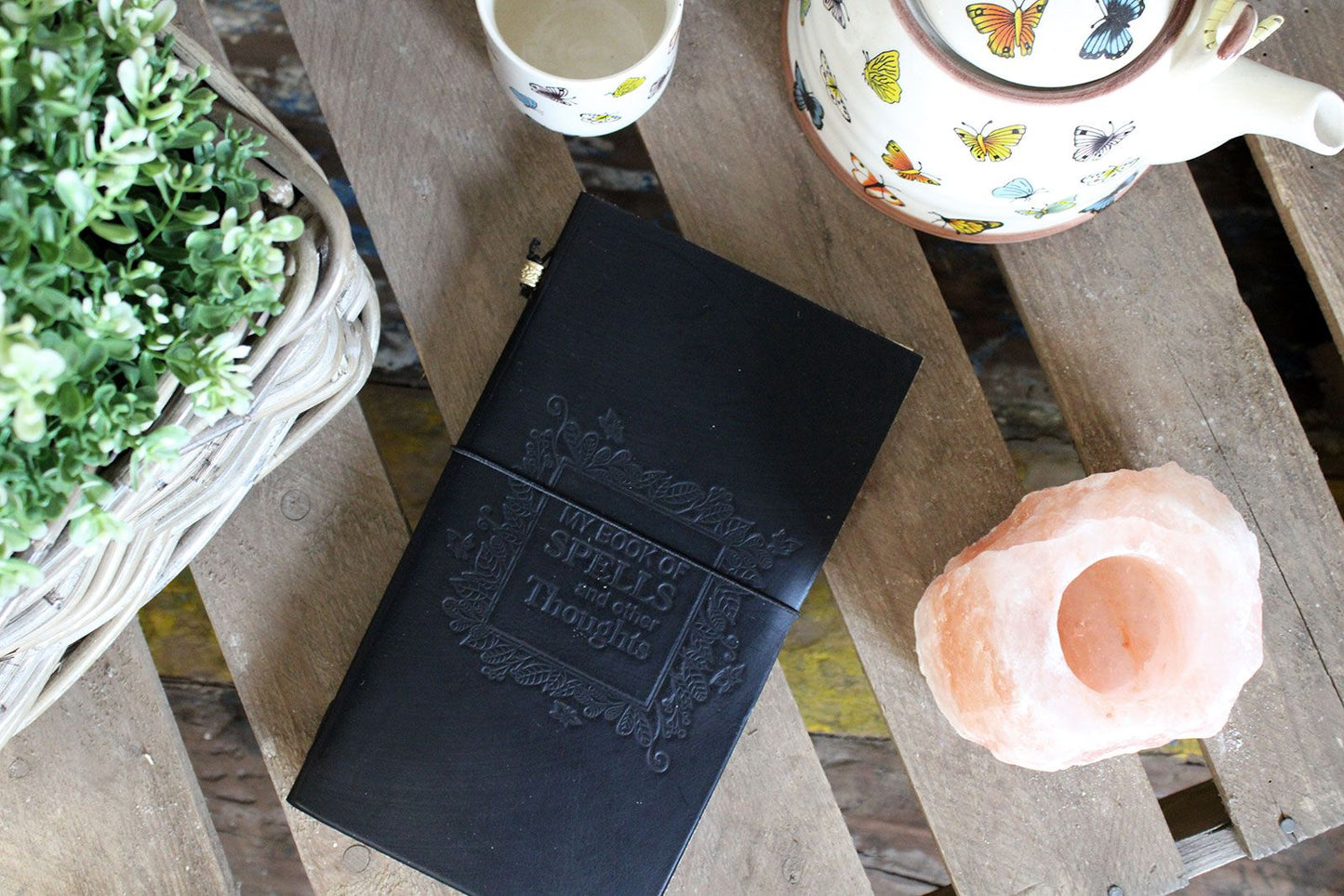 Alt Tag: Handcrafted Leather Journal – My Book of Spells, Black on wooden table with teapot, cup and plant