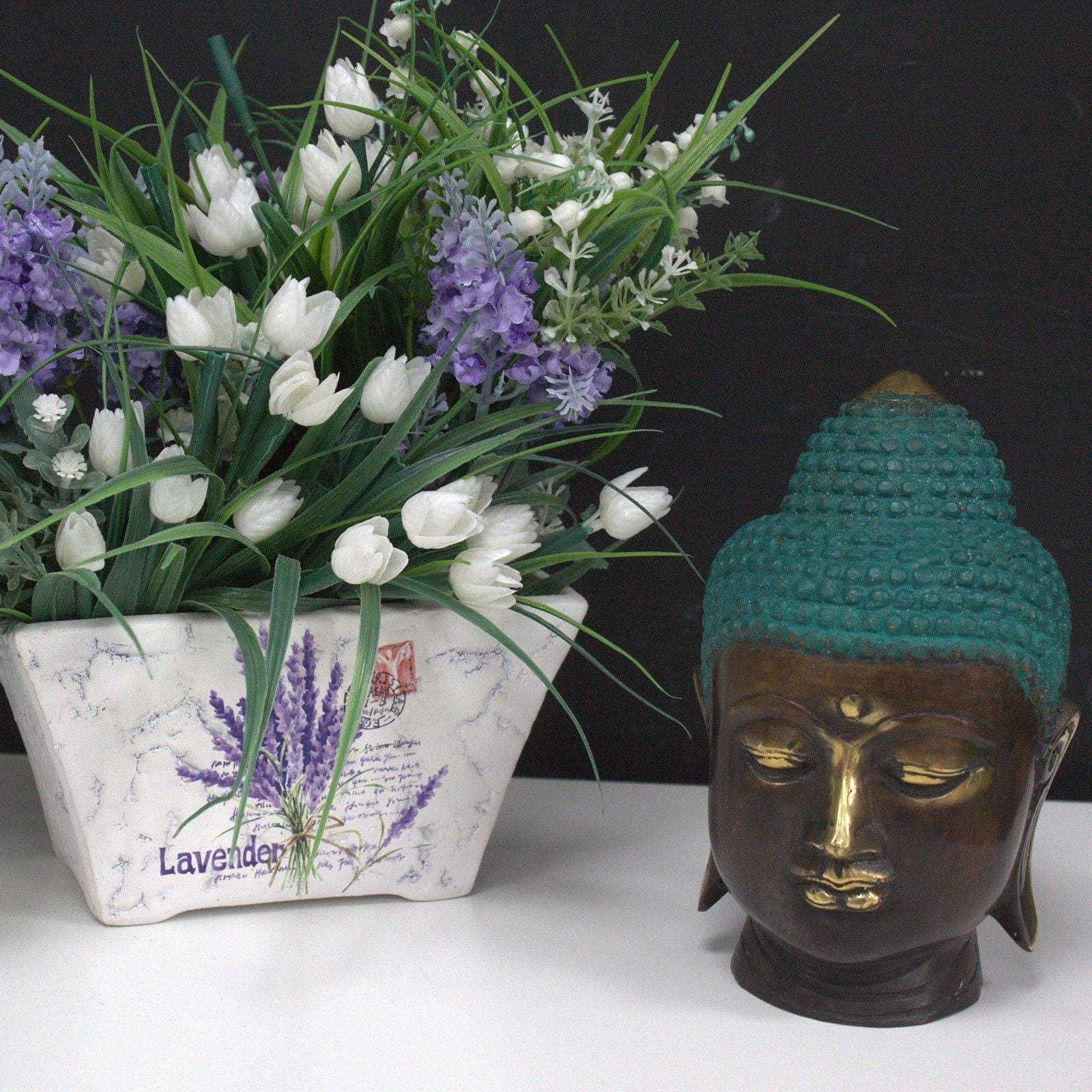 Cabeza de Buda de latón hecha a mano – 15x7x6 CM como decoración de mesa junto a flores blancas y moradas en maceta de cerámica