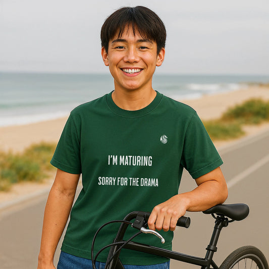 I’m Maturing Teen Sustainable Unisex Tee green t-shirt on teen model by beach, text reads "I’M MATURING SORRY FOR THE DRAMA"