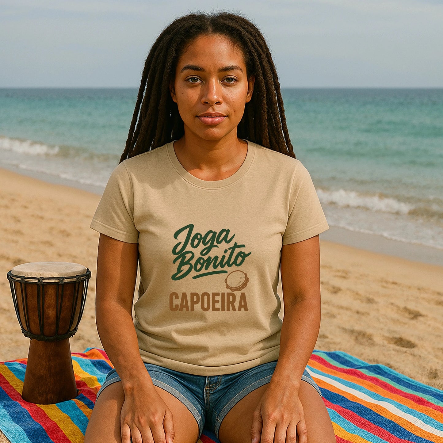 Joga Bonito Capoeria Sustainable Unisex Tee worn by woman sitting on beach, Joga Bonito capoeira graphic print on tan t-shirt
