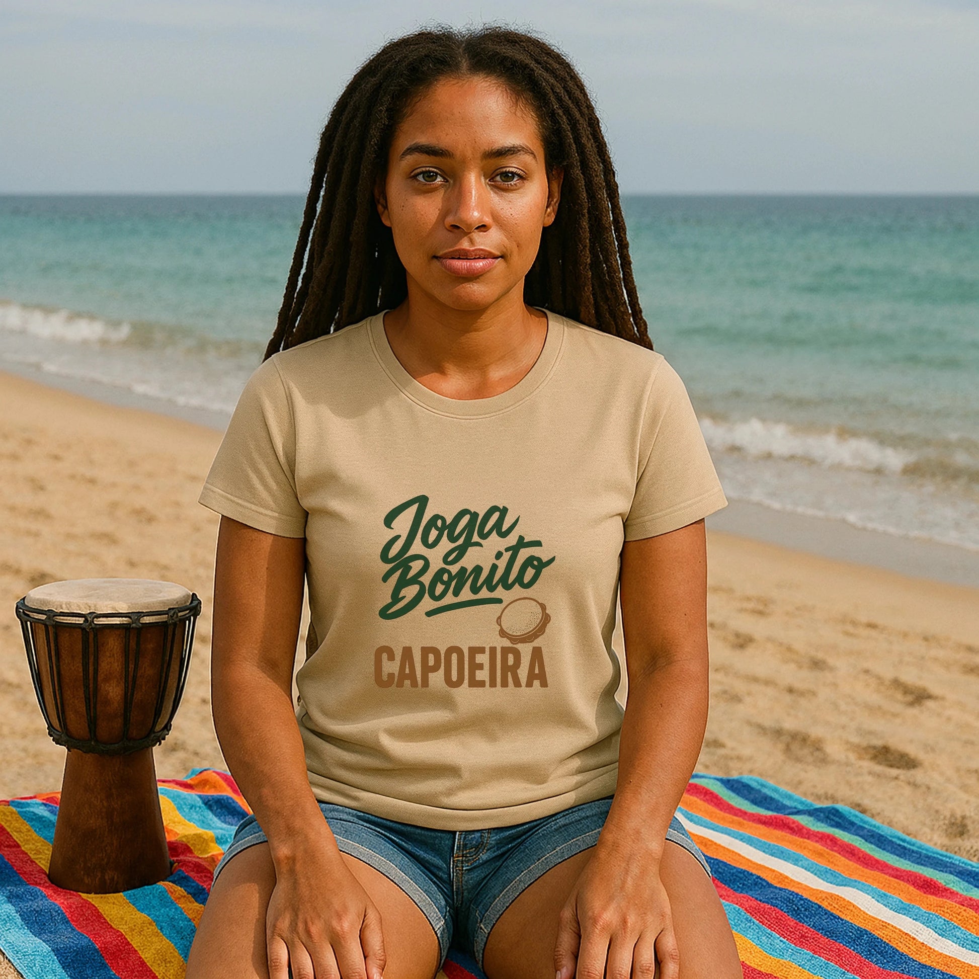 Joga Bonito Capoeria Sustainable Unisex Tee worn by woman sitting on beach, Joga Bonito capoeira graphic print on tan t-shirt