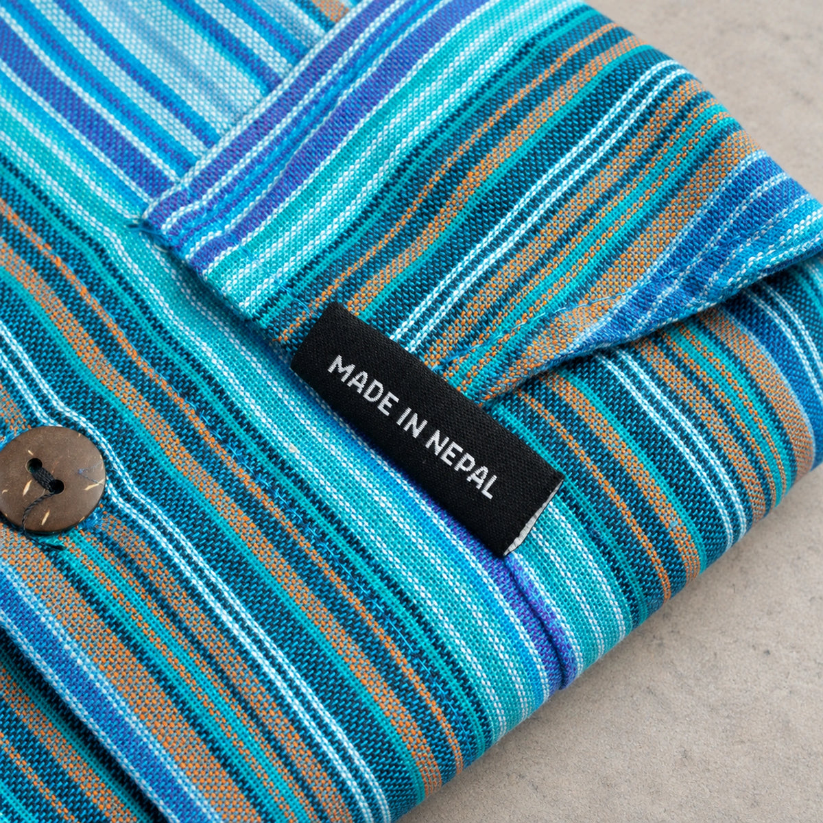 Close-up of the black tab reading MADE IN NEPAL beside the stitched edge of the turquoise striped fabric.