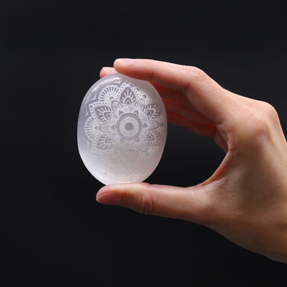 Alt Tag: Mandala-Engraved Selenite Stone – 7x5x2 CM, oval palm stone with mandala engraving held in hand, translucent selenite
