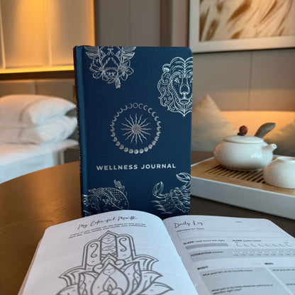 Midnight Blue Journal – Silver Zodiac, 120 Pages midnight blue wellness journal with silver zodiac cover on table, open pages in foreground