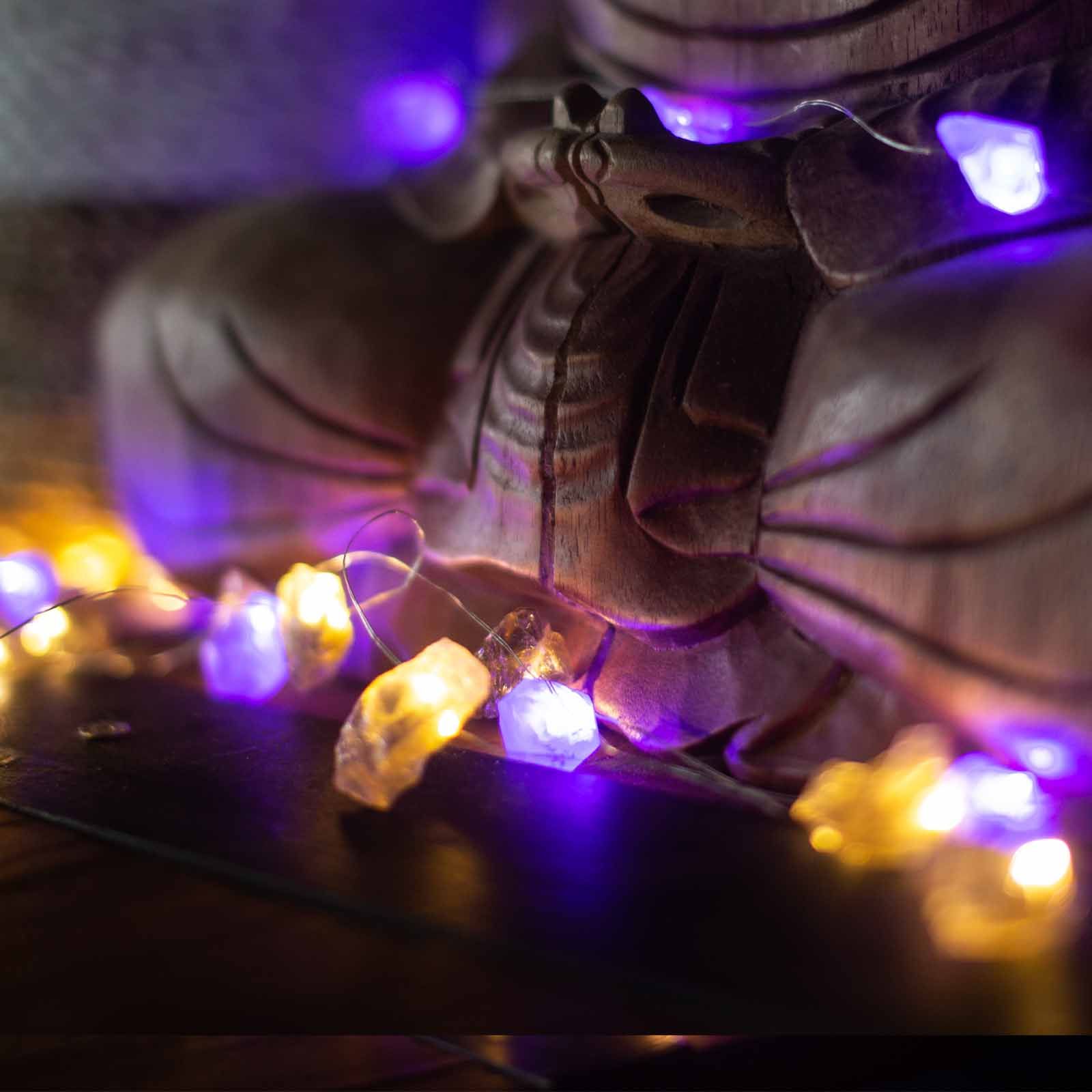 Alt Tag: Mixed Rocks Gemstone Enchantment Lights – Decorative String with warm yellow and purple gemstone bulbs beside a Buddha statue