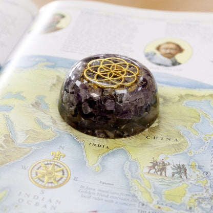 Alt Tag: Mystic Amethyst Orgonite Dome – 6.5x3 CM con chips de amatista y símbolo geométrico dorado, sobre un mapa en escritorio