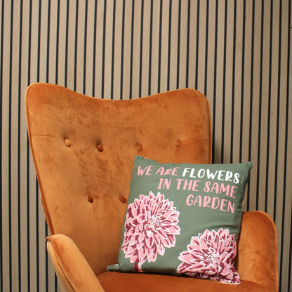 Funda de cojín de algodón natural – 45x45 CM con el texto “We Are Flowers” y estampado floral rosa sobre cojín verde, ambientado en una silla naranja