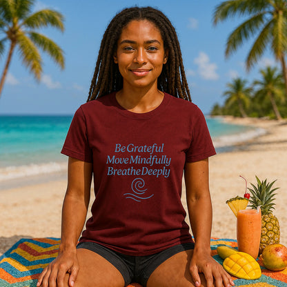 Yoga 100% Organic Cotton T-Shirt on woman sitting on beach, burgundy tee with "Be Grateful Move Mindfully Breathe Deeply" print