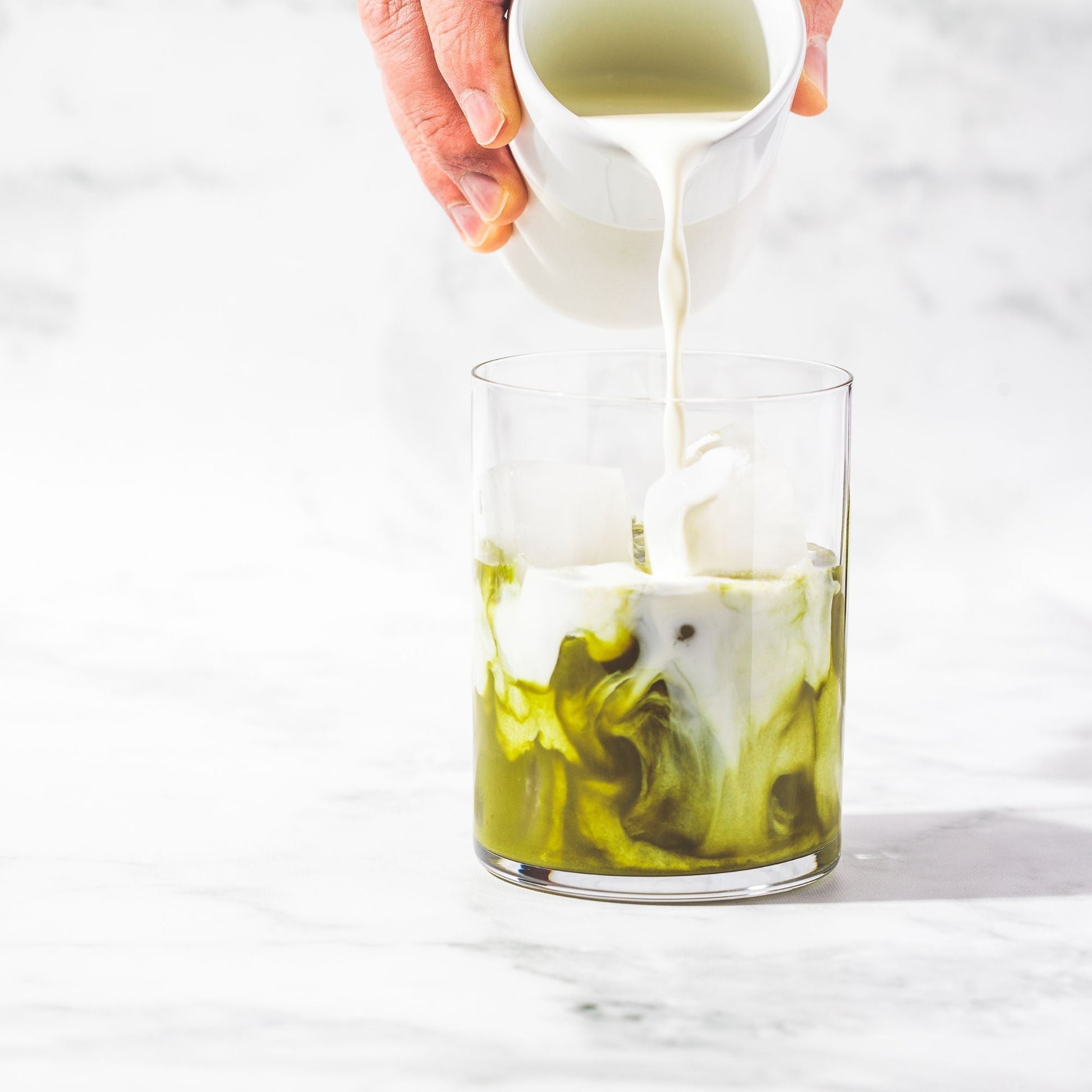 Organic Culinary Matcha Tea – 50 g latte with milk being poured into iced green matcha in a clear glass