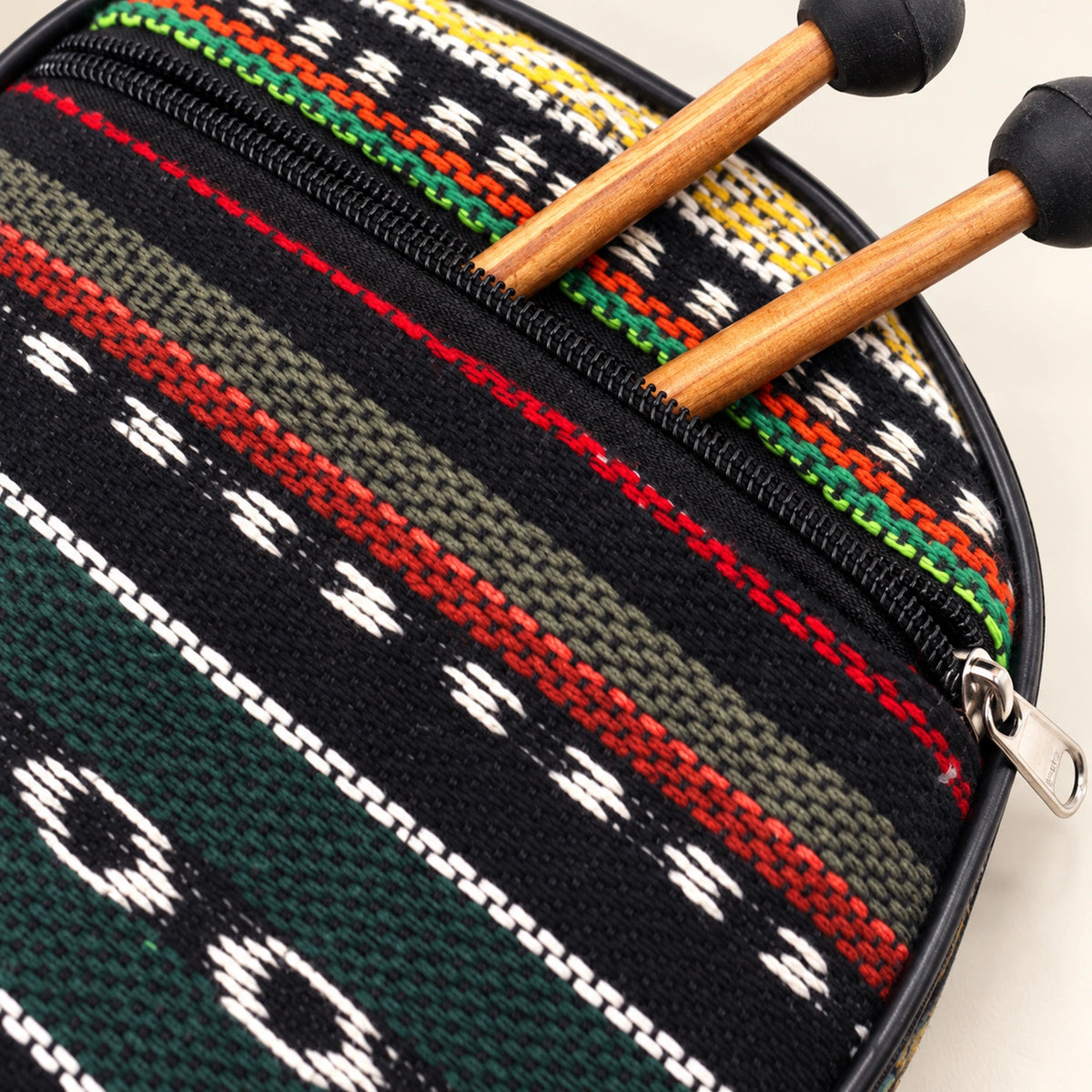 Close view of the patterned outer pocket, black zipper, silver-coloured pull and two wooden mallet shafts entering the pocket.