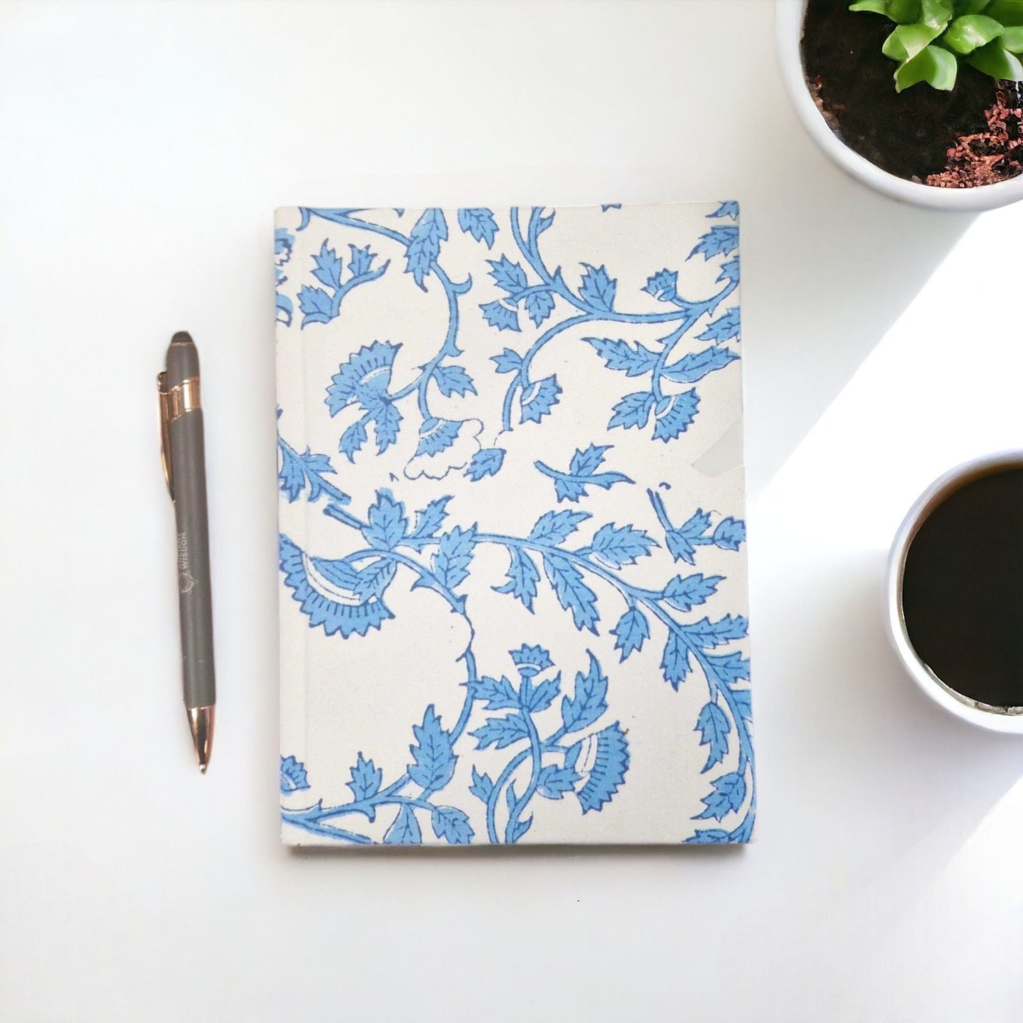 Alt Tag: Pale Blue Floral Cotton Notebook – 20x15 CM, handcrafted cotton cover with blue floral pattern and handmade paper, on desk with pen and coffee