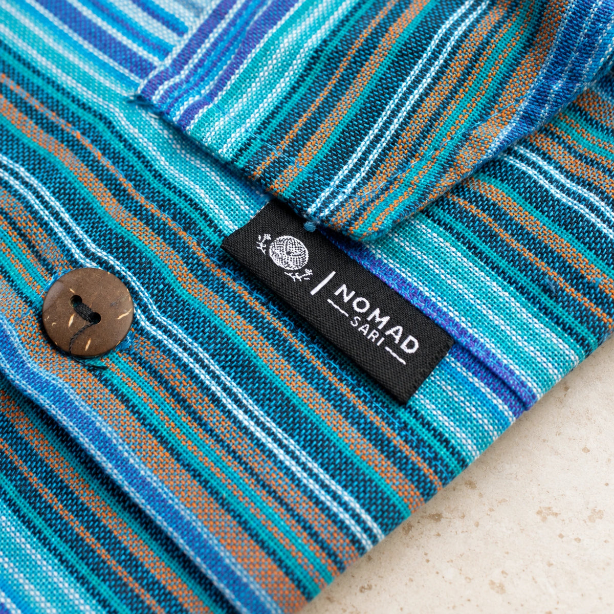 Detail of the striped pocket flap with its brown button, visible stitching and black Nomad Sari brand tab.