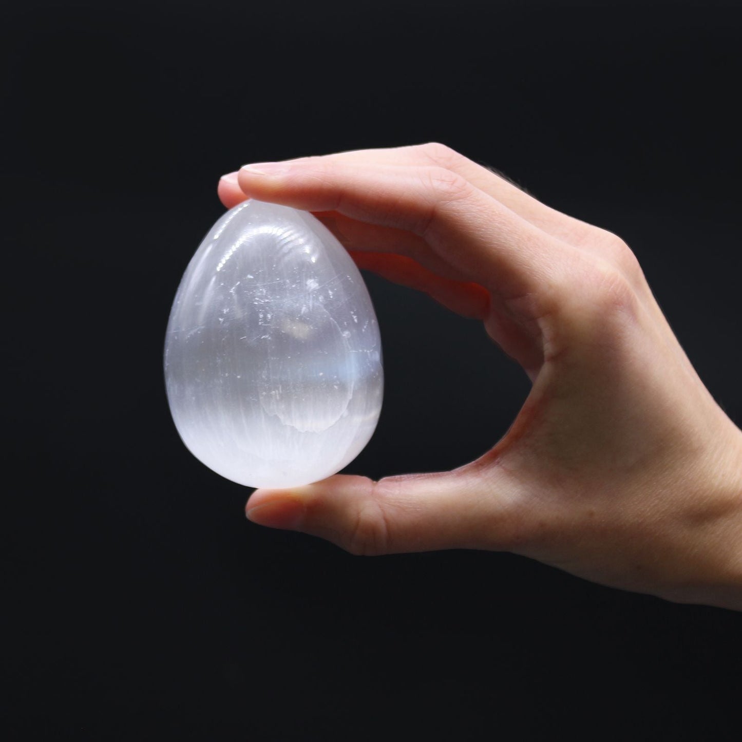 Alt Tag: Polished Selenite Egg – 5-6 CM sostenido en la mano, cristal blanco pulido en forma de huevo sobre fondo negro