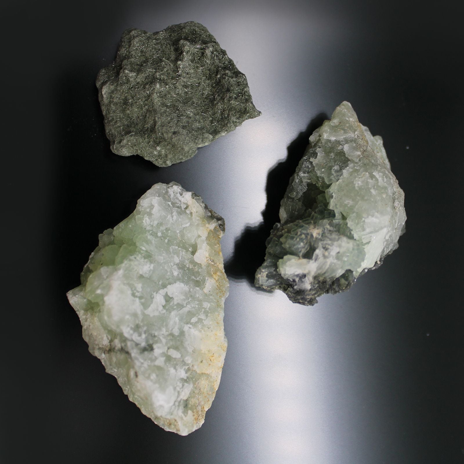 Alt-Tag: Prehnit-Mineralproben – Ca. 100 Stück, drei rohe, gelbgrüne Prehnit-Proben auf dunklem Hintergrund