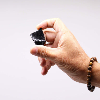 Raw Crystals (500gm) - Black Obsidian, mano sosteniendo cristal de obsidiana negra en bruto con acabado brillante