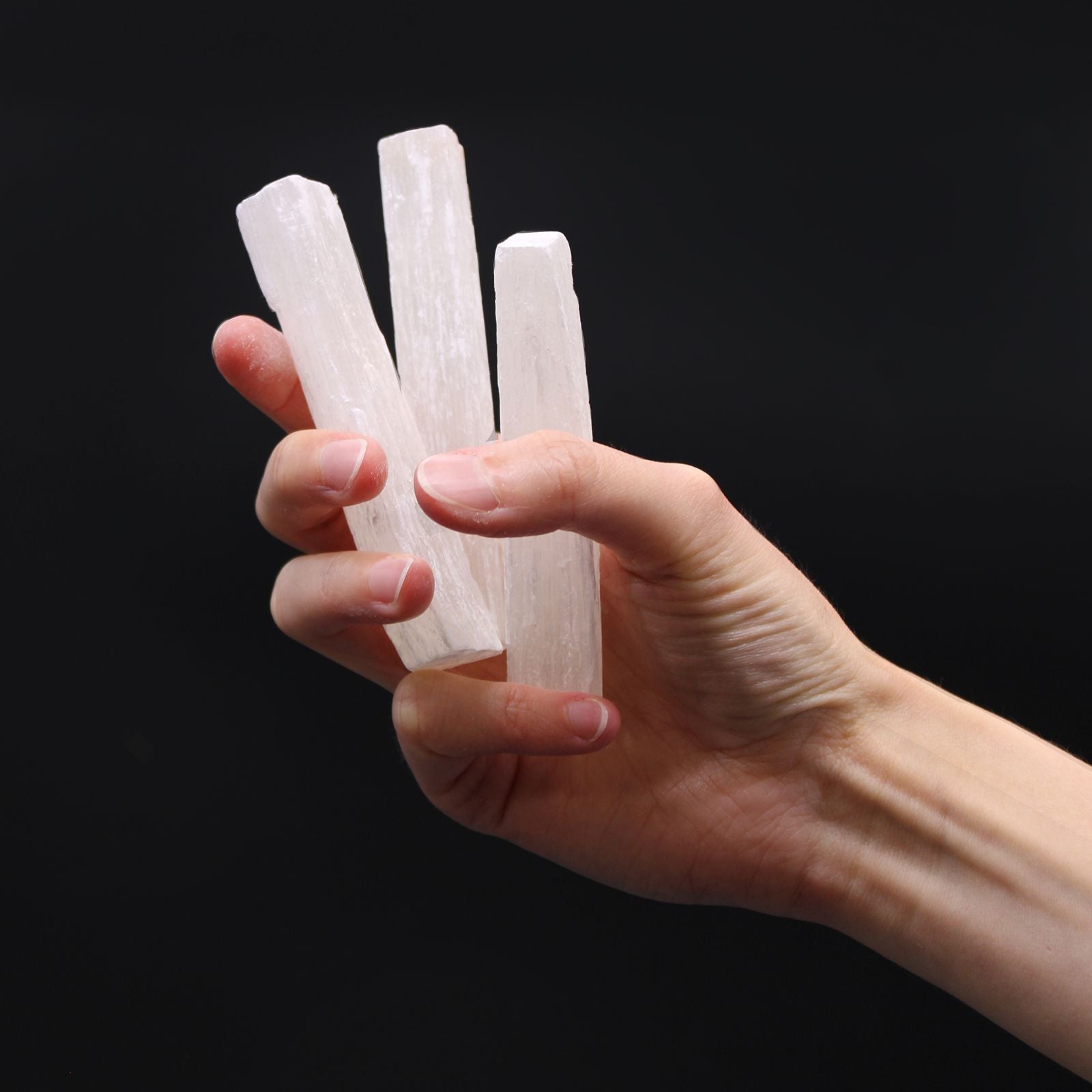 Alt Tag: Raw Selenite Crystal Wand – 7-10 CM, varitas de selenita cruda translúcidas sostenidas en la mano sobre fondo negro
