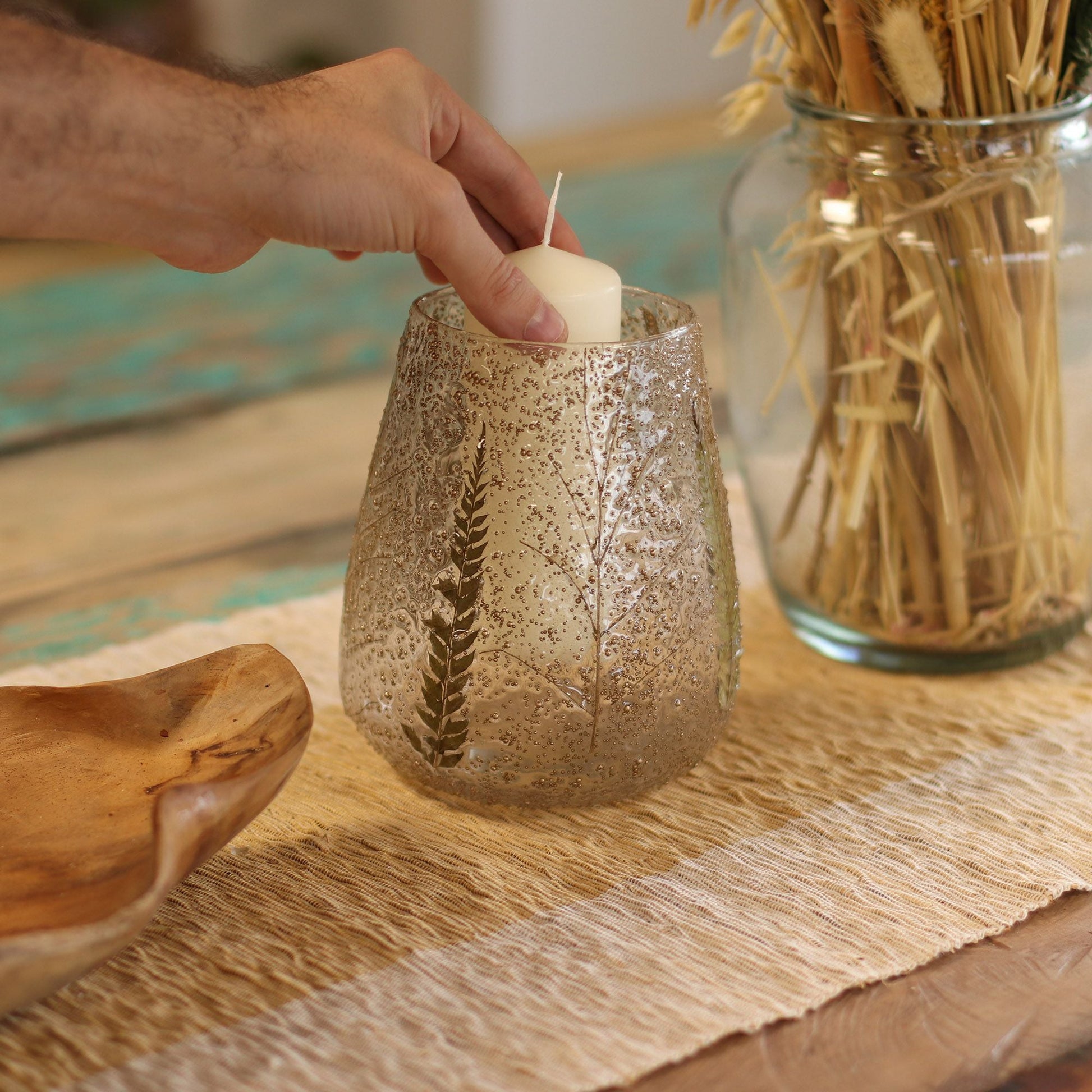 Alt Tag: Portavelas de vidrio reciclado – Grande 15x12 CM con textura de hoja de helecho, mano colocando una vela tipo tealight sobre una mesa rústica decorada