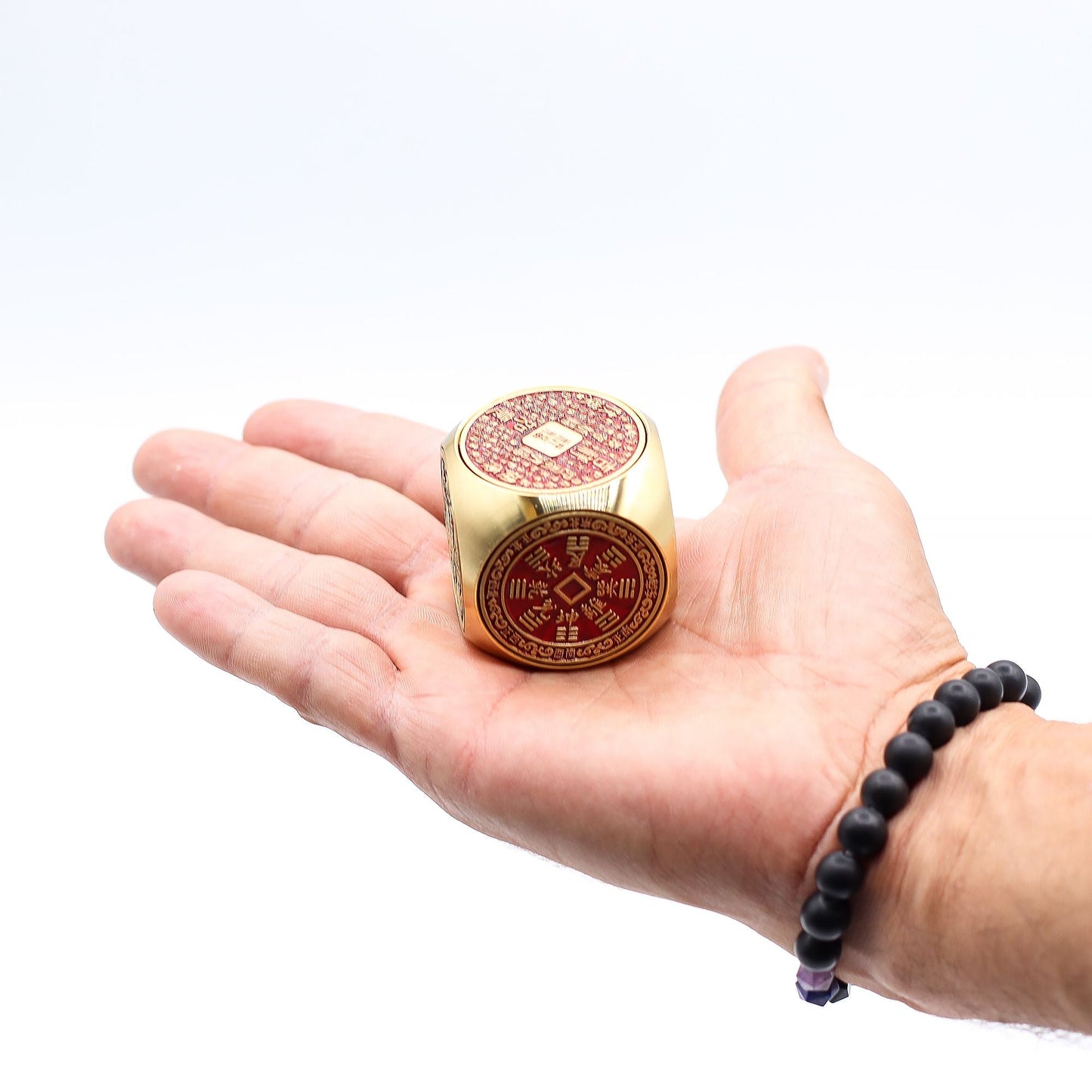 Alt Tag: Red Brass Prosperity Spinner – 4x4 CM en mano, cubo de latón rojo con símbolos decorativos, vista frontal y superior