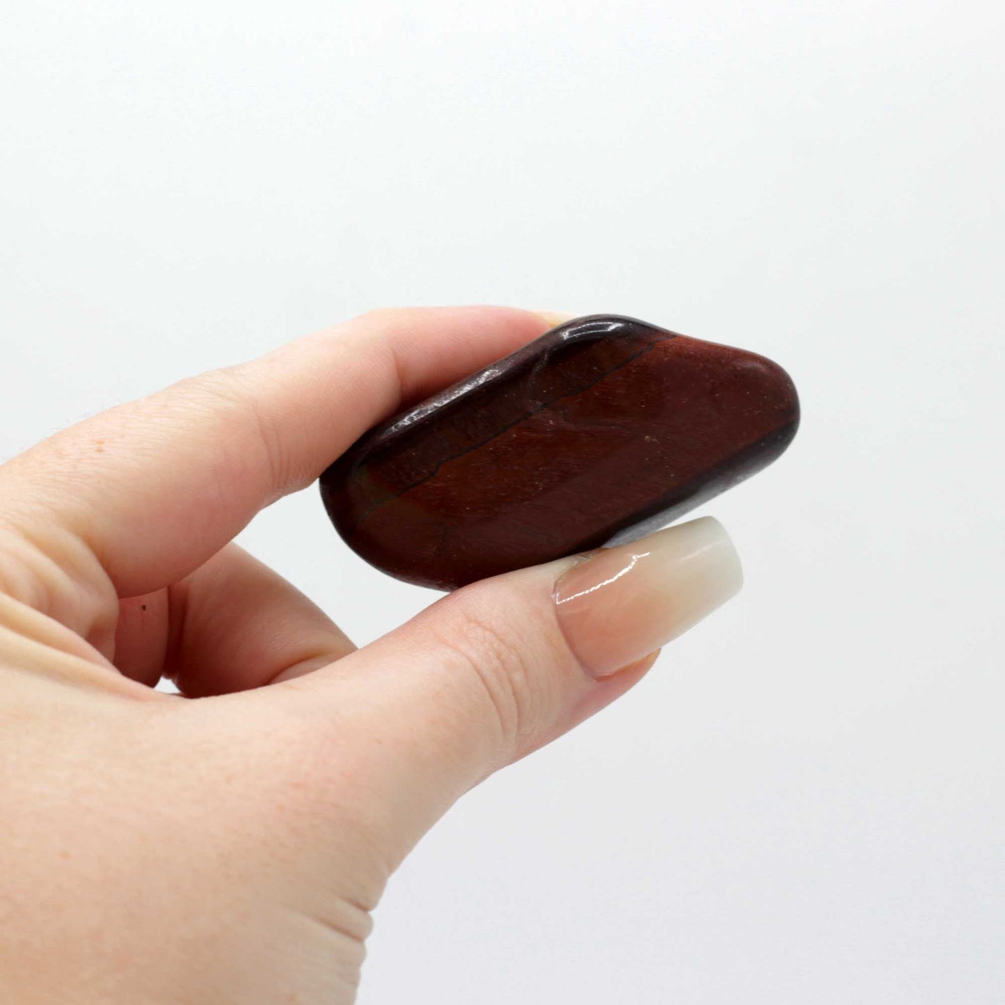 Alt Tag: Gemstone Tigers Eye – Red Tumble Stone 30MM held in hand, polished red-brown tiger’s eye gemstone with smooth tumble finish
