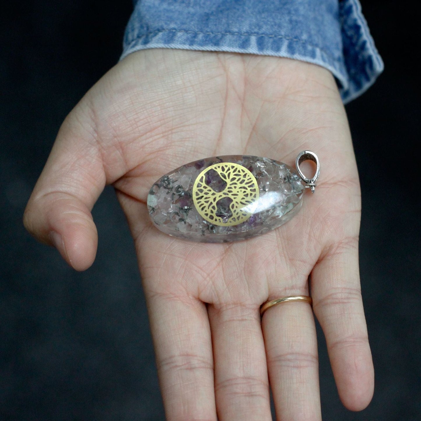 Alt Tag: Resin & Gemstone Orgonite Pendant – 7 Chakra Oval Tree, colgante ovalado de resina con gemas y símbolo árbol dorado, en mano