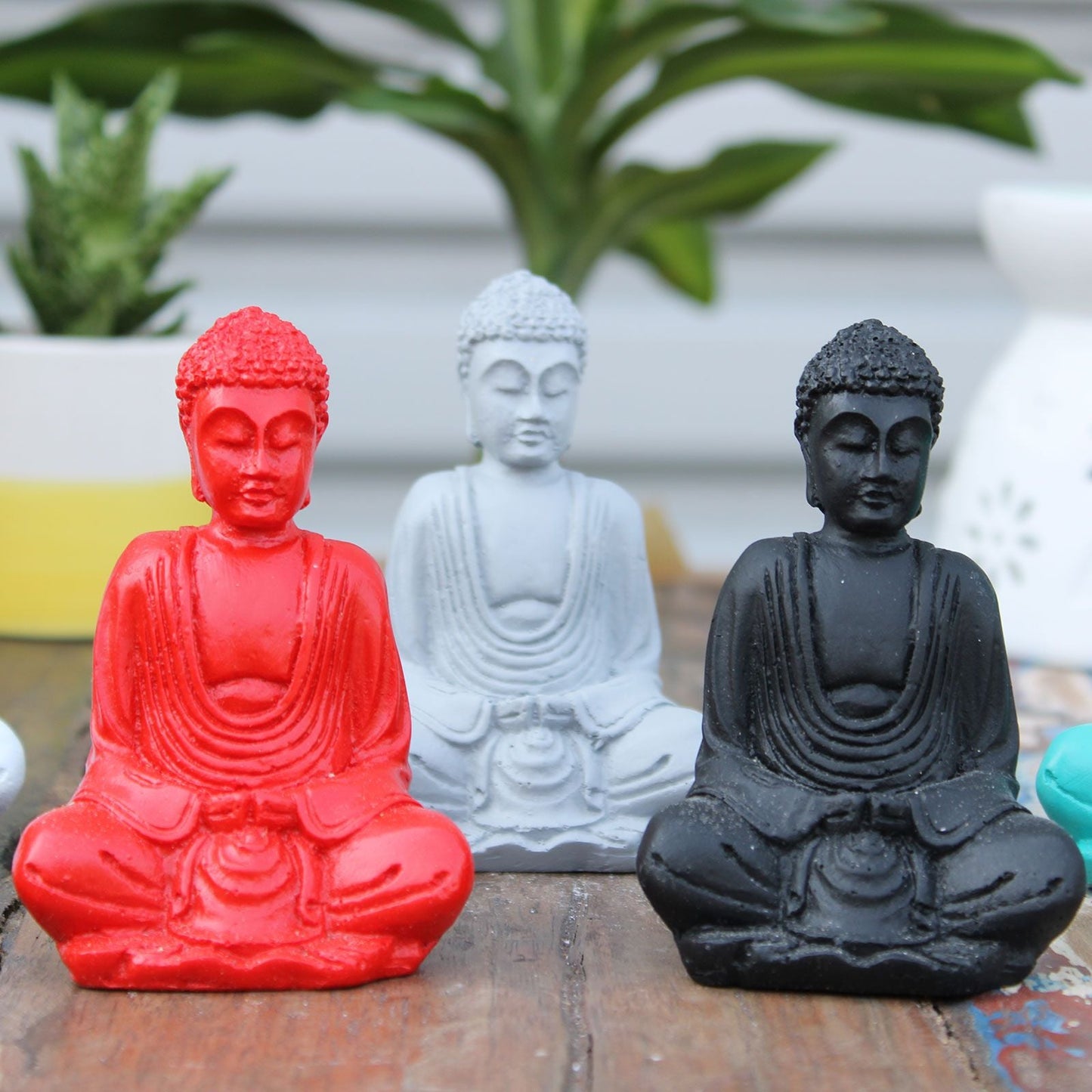 Alt Tag: Mini Buda de resina pintado a mano – figuritas de mini Buda en colores surtidos (rojo, blanco y negro) de resina, sentado sobre una superficie de madera