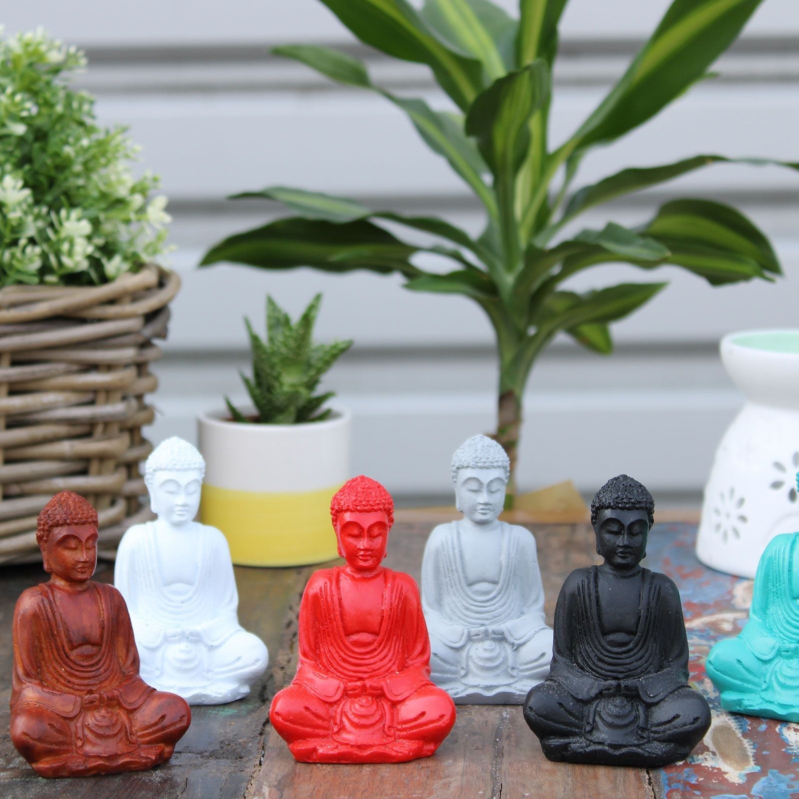 Mini Buda pintado a mano en resina – Colores surtidos set de pequeñas figuras de Buda sentado en rojo, blanco, negro y verde azulado sobre una mesa