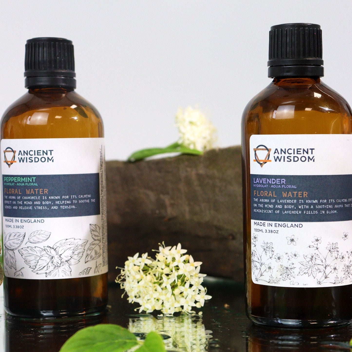 Revitalizing Peppermint Hydrolat – 100ML botella de agua floral de menta en frasco ámbar con etiqueta Ancient Wisdom, junto a flores blancas