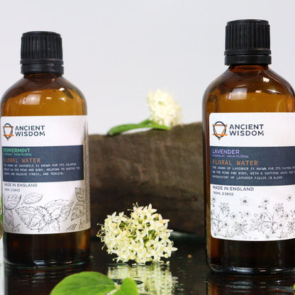 Revitalizing Peppermint Hydrolat – 100ML botella de agua floral de menta en frasco ámbar con etiqueta Ancient Wisdom, junto a flores blancas