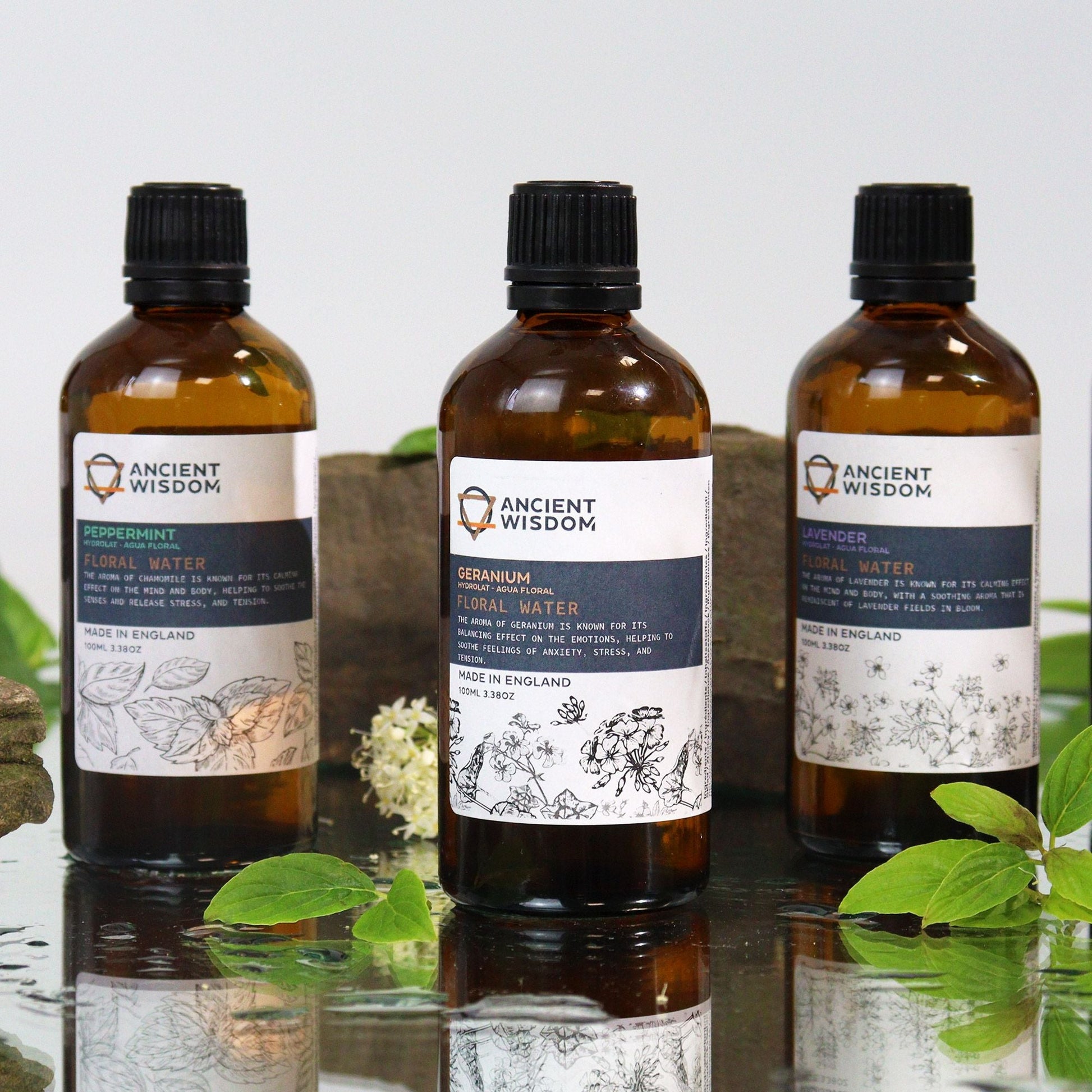 Revitalizing Peppermint Hydrolat – 100ML en botella ámbar con etiqueta peppermint floral water, junto a otras aguas florales y hojas verdes