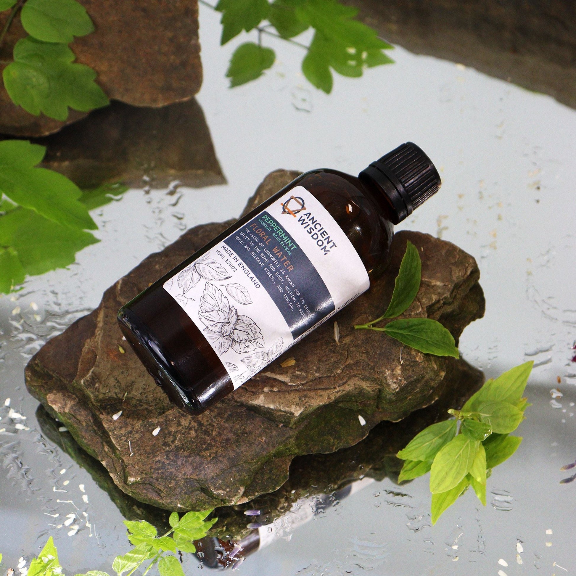Alt Tag: Revitalizing Peppermint Hydrolat – 100ML en frasco ámbar sobre piedras con hojas verdes, agua floral de menta piperita 100 ml