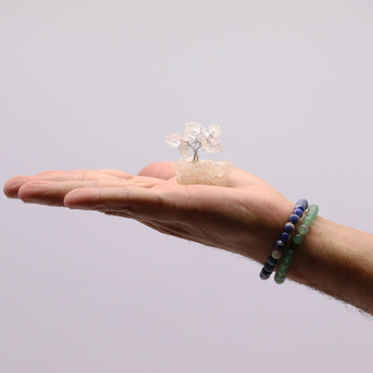 Rock Quartz Mini Gemstone Tree – 15 Stones on a hand holding a small clear quartz gemstone tree with orgonite base, 5 cm tall