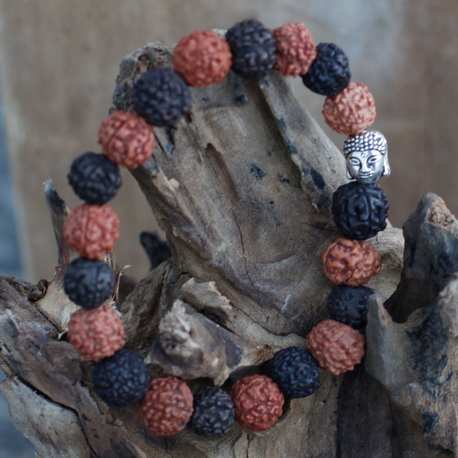 Alt Tag: Rudraksha Buddha Bangle Mala – Mix Beads-armband med blandade rudraksha-pärlor och en Buddha-berlock i silverton på träbakgrund