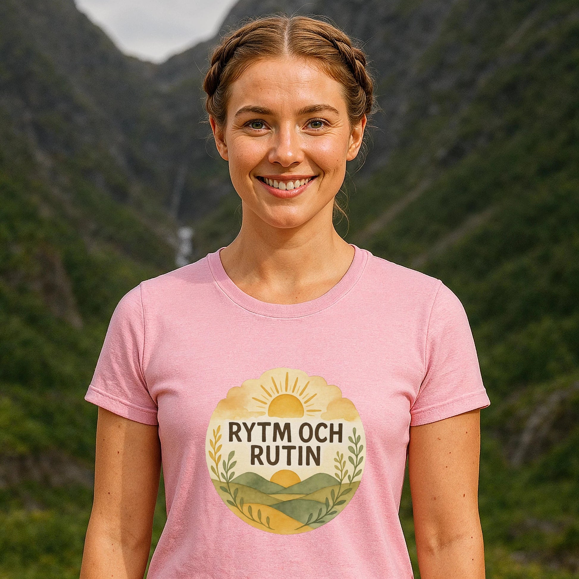 Alt Tag: Rytm Rutin Bomulls Premium Unisex T-Shirt rosa med "RYTM OCH RUTIN"-tryck, modell utomhus framför bergslandskap