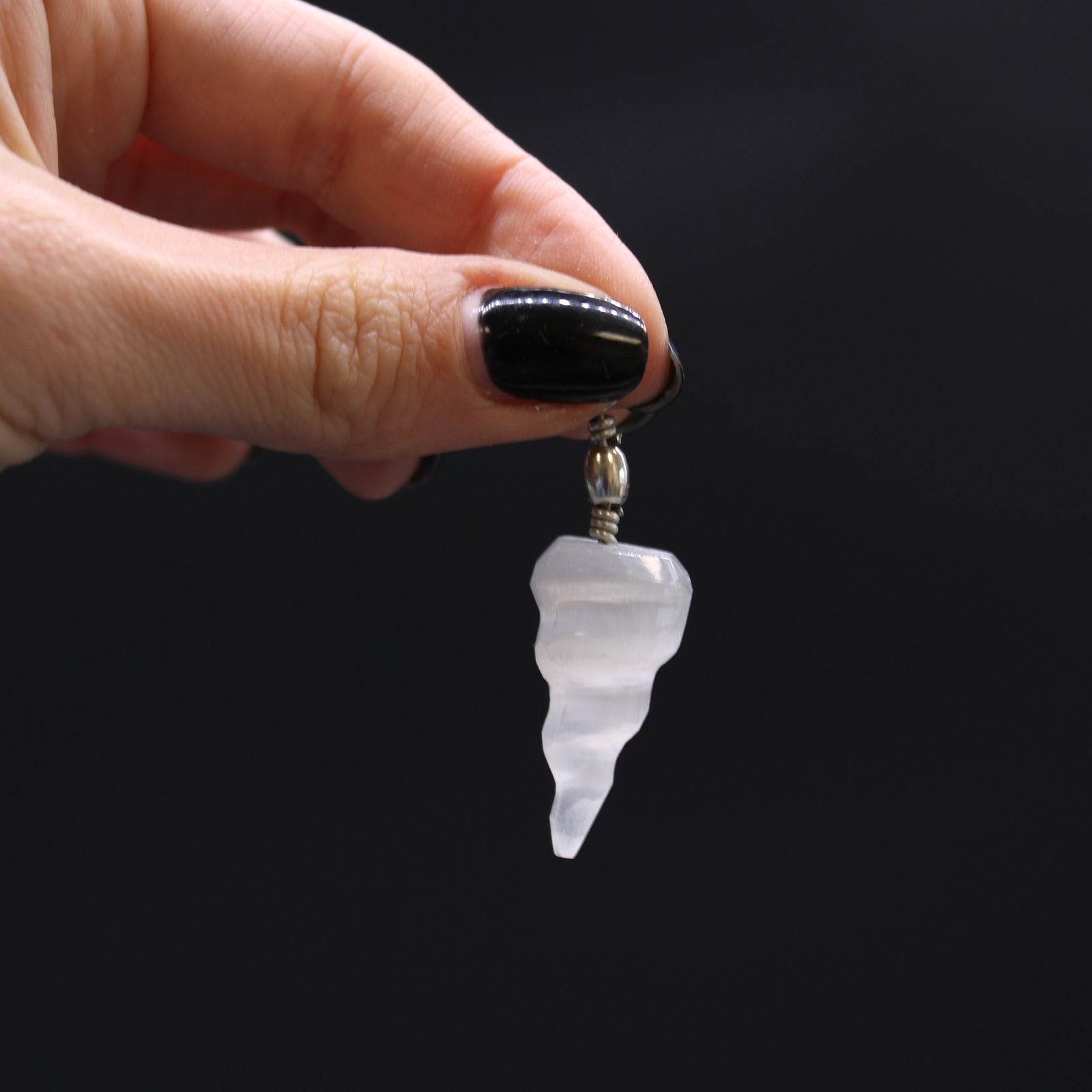 Selenit-Spiralanhänger – 4x1,5 CM transluzenter Selenit-Spiralanhänger-Charm, in der Hand gehalten vor schwarzem Hintergrund