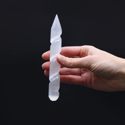 Hand holding Selenite Spiral Wand – 16 CM Pointed End, polished spiral selenite crystal wand with pointed tip on black background