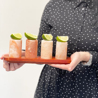 Set med 4 Himalayan Salt shotglas med serveringsställ i trä på träbricka med limeklyftor, hålls av en person
