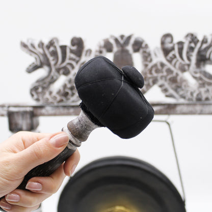 Small Harmonizing Gong in Stand – 25 CM – Black striker mallet held by hand in front of black gong and carved wooden stand
