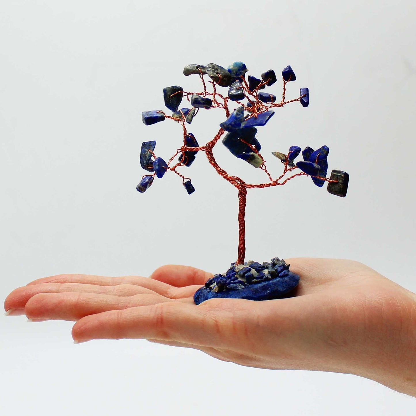 Alt Tag: Sodalite Gemstone Tree – 35 Stones on Blue Agate handcrafted wire tree with blue gemstone chips on agate base in hand