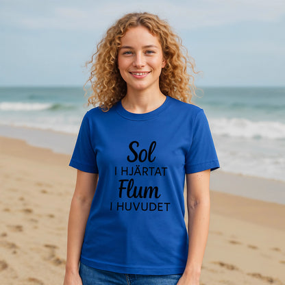 Alt Tag: Model wearing Sol I Hjärtat Flum I Huvudet 100% Organic Cotton T-Shirt, blue tee with black text print on beach